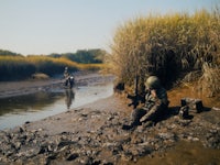 a soldier is sitting in the mud next to a river